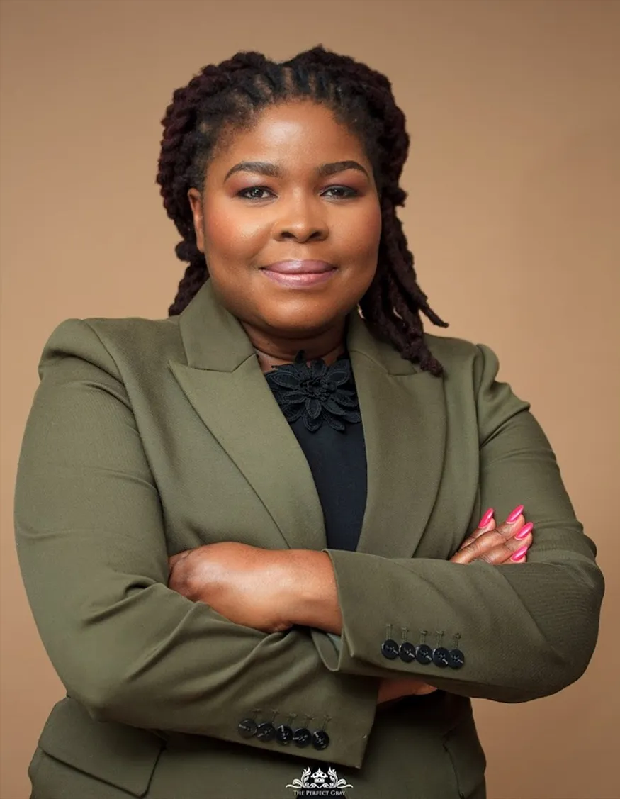 A Linea Consulting adviser in an olive-green blazer, arms folded, photographed against a warm studio background.